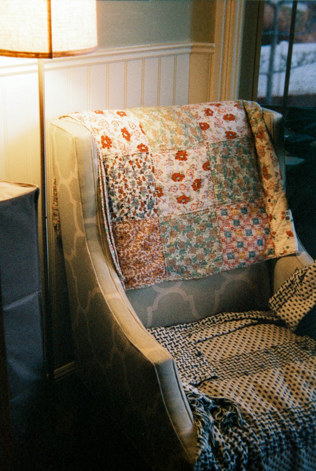 Armchair with patterned quilt and blanket draped.